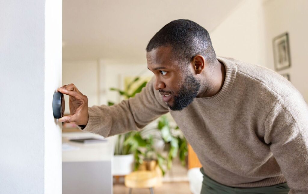 Worried homeowner near a thermostat turning off/down a thermostat